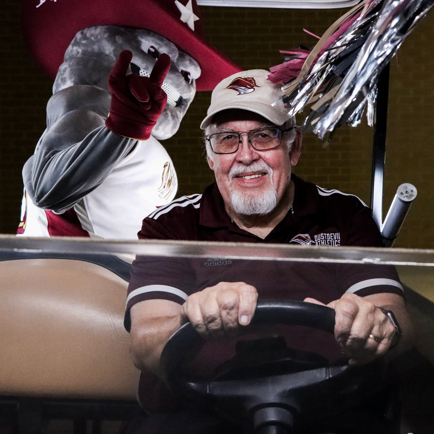 Dr. Pablo Arenaz smiling while driving a golf cart with Dusty the Dustdevil