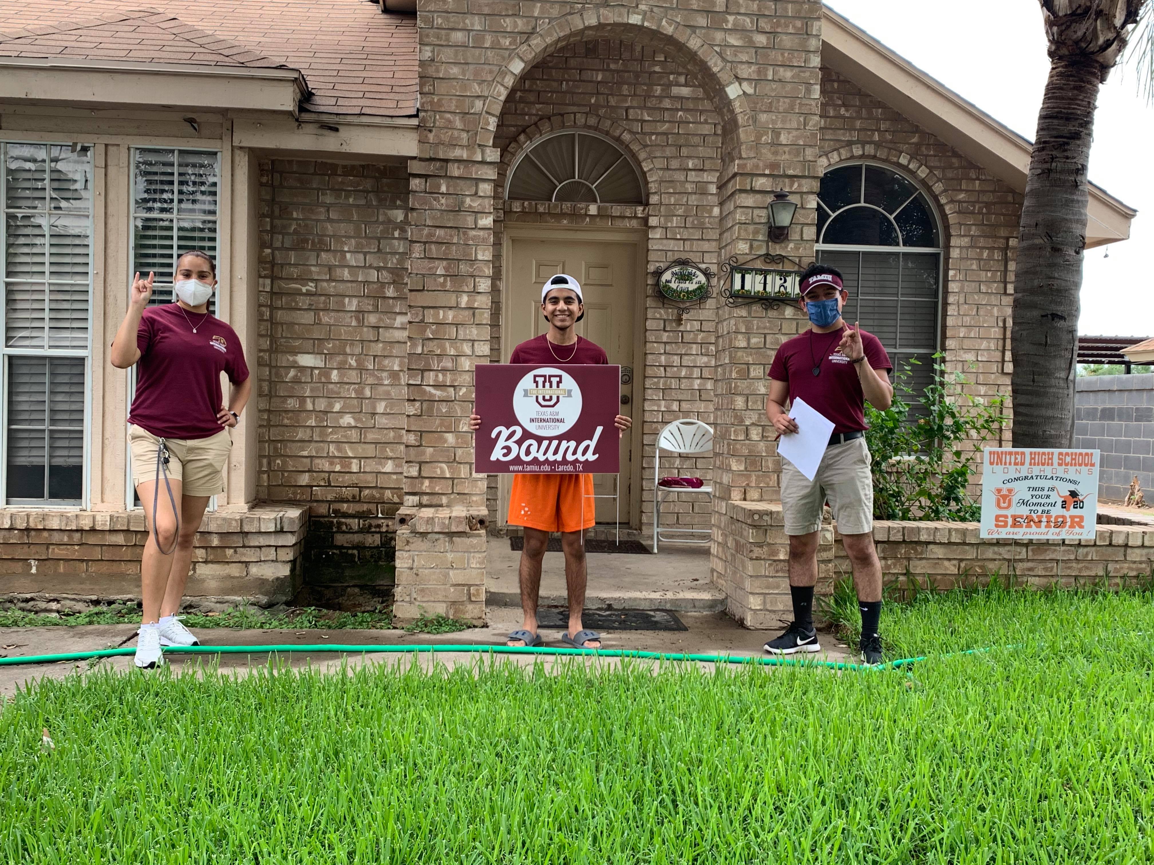 Texas A&M International University freshman student Jared Nava (center) holds his brand new “TAMIU Bound” lawn sign. A lawn sign and welcome packet were brought to him by New Student Orientation Leaders Yamile Vasquez (left) and Daniel Perez (right).