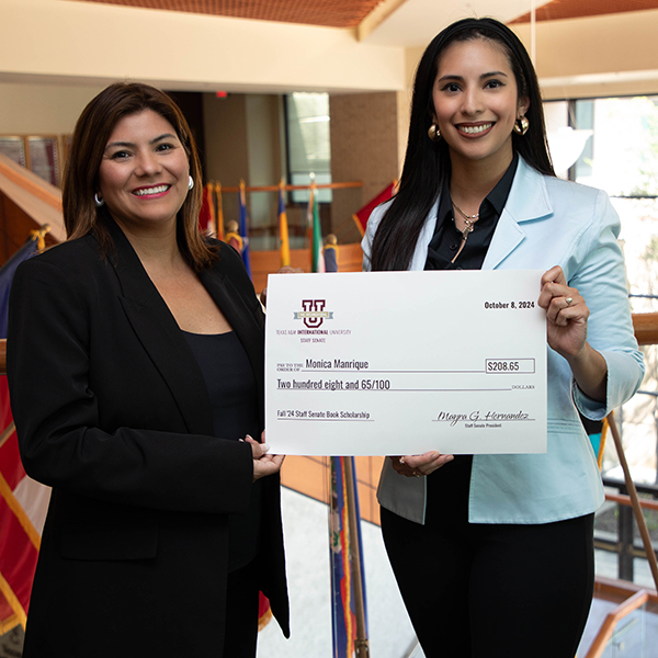 Monica Manrique given a check by Staff Senate President Mayra Hernandez